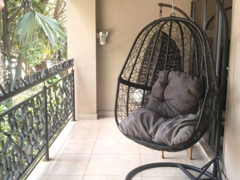 A covered balcony featuring tiled flooring and a decorative wrought iron balustrade, overlooking a lush garden area.