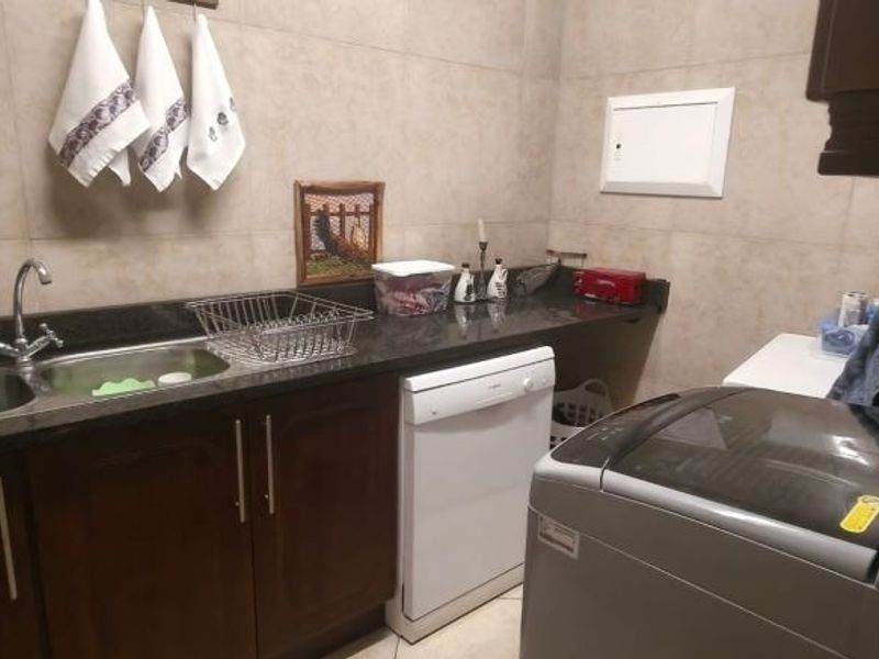 A functional laundry room featuring dark wood cabinetry, granite countertops, a double stainless steel sink, and tiled wall finishes.
