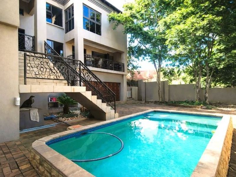 Rear exterior view featuring a swimming pool, paved patio area, and an external wrought iron staircase leading to the upper level.