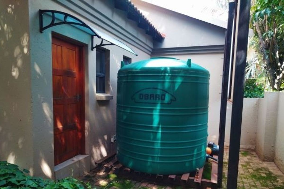 Rear exterior area featuring a large green water storage tank with an integrated pump system and a timber access door with a protective canopy.