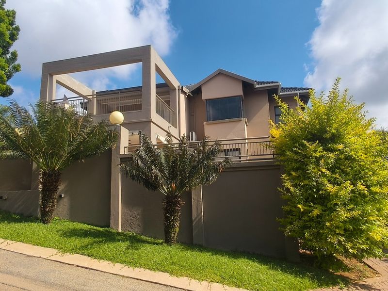 A well-maintained multi-level residential property featuring a prominent balcony, secure boundary walls, and a paved driveway entrance.