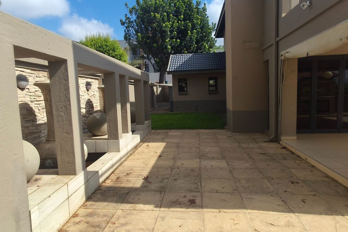 Rear exterior view featuring a paved patio area with a decorative stone wall, integrated water feature, and a retractable blind for shade.