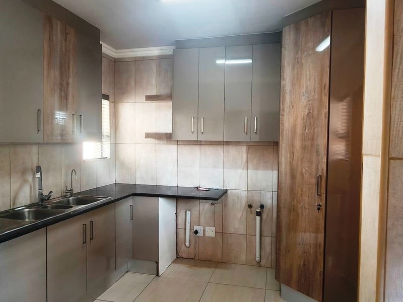 A clean, modern kitchen featuring wood-grain and grey cabinetry, dark countertops, a double basin sink, and full-height wall tiling.