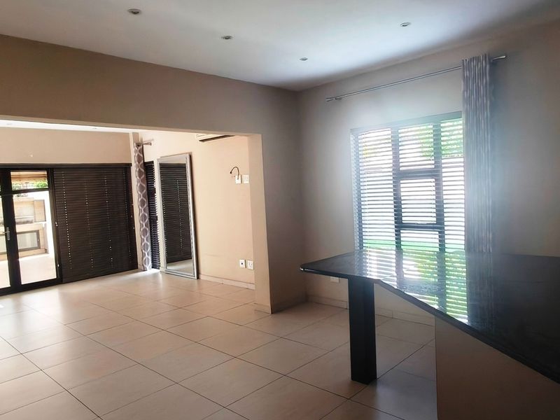 Spacious open-plan living area featuring tiled floors, recessed lighting, a granite breakfast bar, and large sliding doors leading to an outdoor patio.