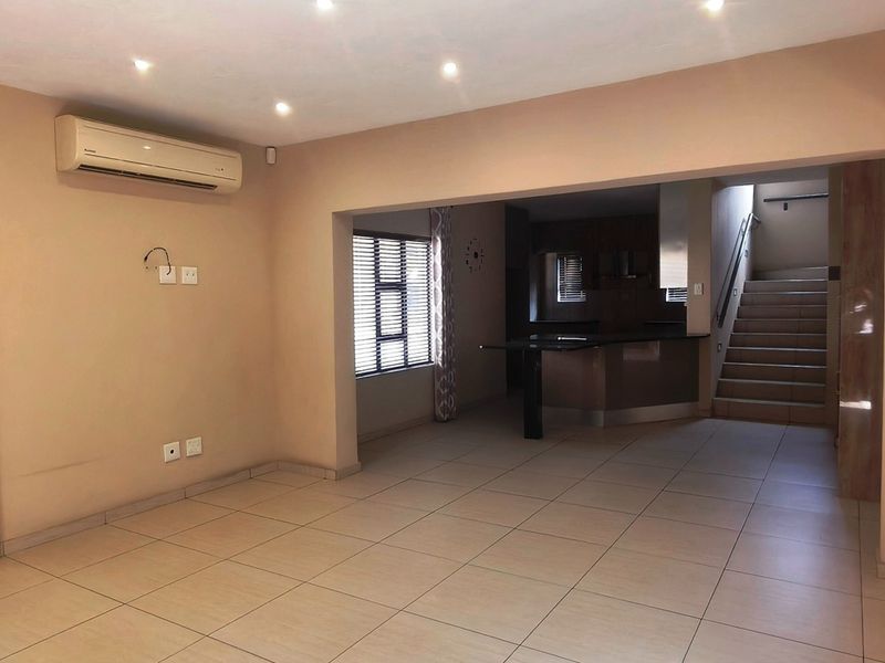 Spacious open-plan living area featuring tiled floors, recessed lighting, air conditioning, and an integrated kitchen with a staircase leading to the upper level.