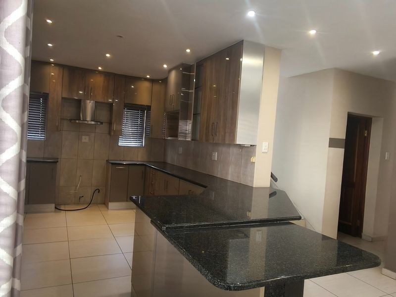 Modern kitchen featuring granite countertops, extensive built-in cabinetry, glass-front display units, and tiled flooring with recessed lighting throughout.