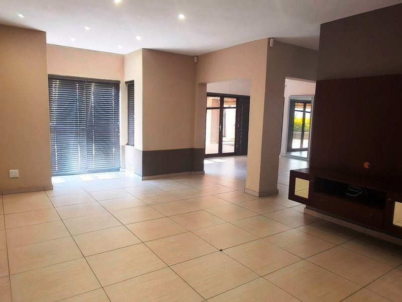Spacious open-plan living area featuring neutral tiled flooring, recessed downlights, and a built-in media console with direct access to outdoor spaces.