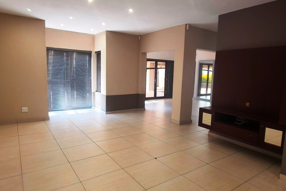Spacious open-plan living area featuring neutral tiled flooring, recessed downlights, and a built-in media console with direct access to outdoor spaces.