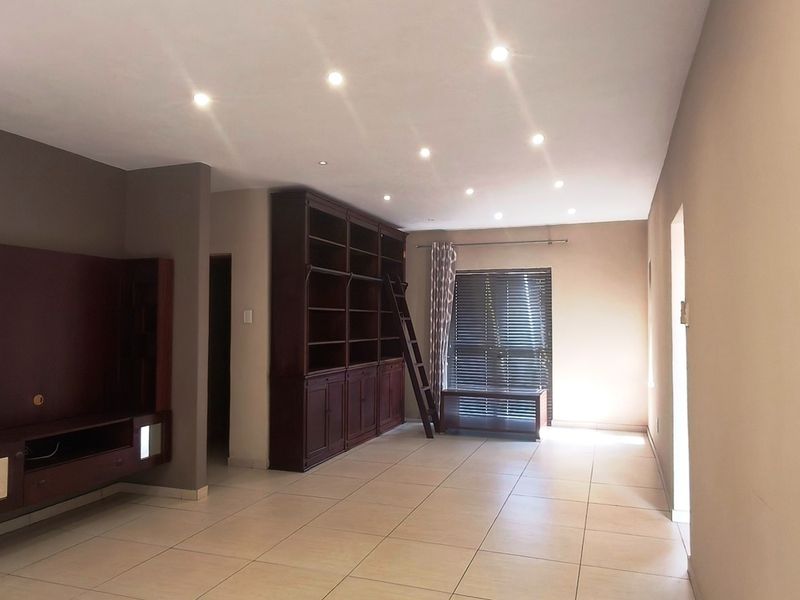 Spacious living area featuring neutral tiled flooring, recessed downlighting, and extensive built-in wooden cabinetry with integrated shelving.