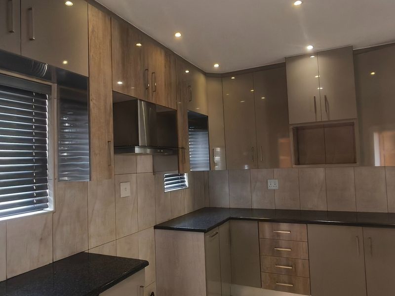 Modern kitchen featuring high-gloss cabinetry, granite countertops, tiled backsplash, and integrated extractor fan with recessed lighting.