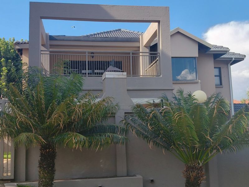 Front elevation of a multi-story residence featuring a prominent upper-level balcony, tiled roofing, and a secure boundary wall with an integrated outdoor fireplace.