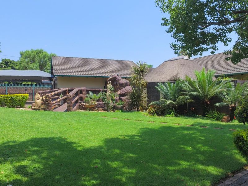 A well-maintained garden featuring a lush green lawn, mature landscaping, a decorative rock feature with a small bridge, and views of the property's exterior.