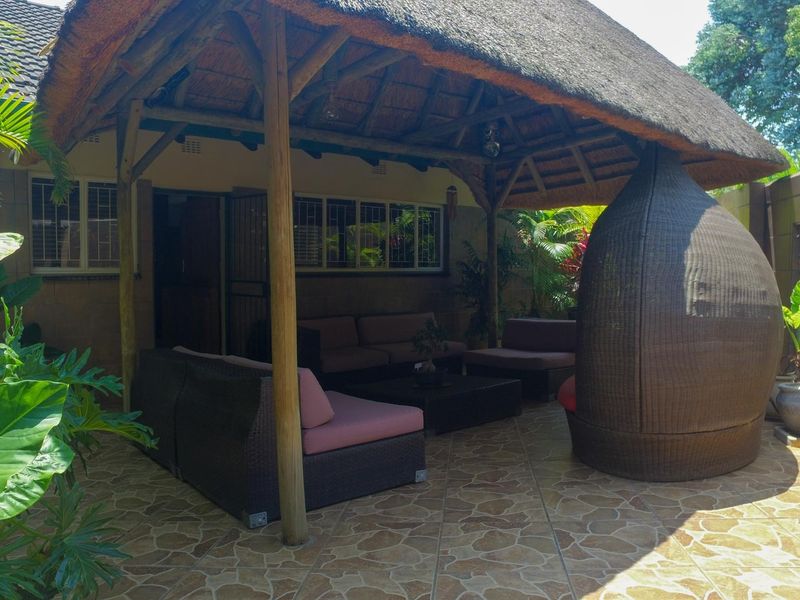 A covered outdoor patio area featuring a traditional thatched roof, timber support beams, and durable tiled flooring, ideal for relaxed outdoor living.