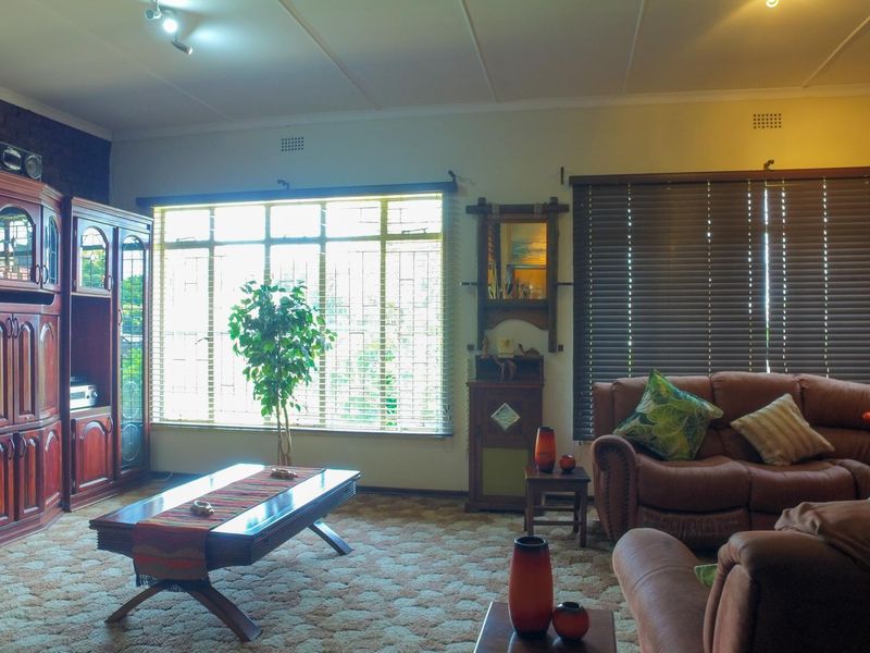 Spacious living room featuring an exposed brick accent wall, built-in cabinetry, and large windows with venetian blinds, offering a traditional layout.
