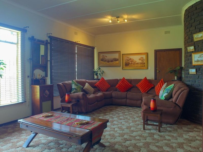 Spacious living room featuring a prominent brick fireplace, large windows with venetian blinds, and patterned carpet flooring.