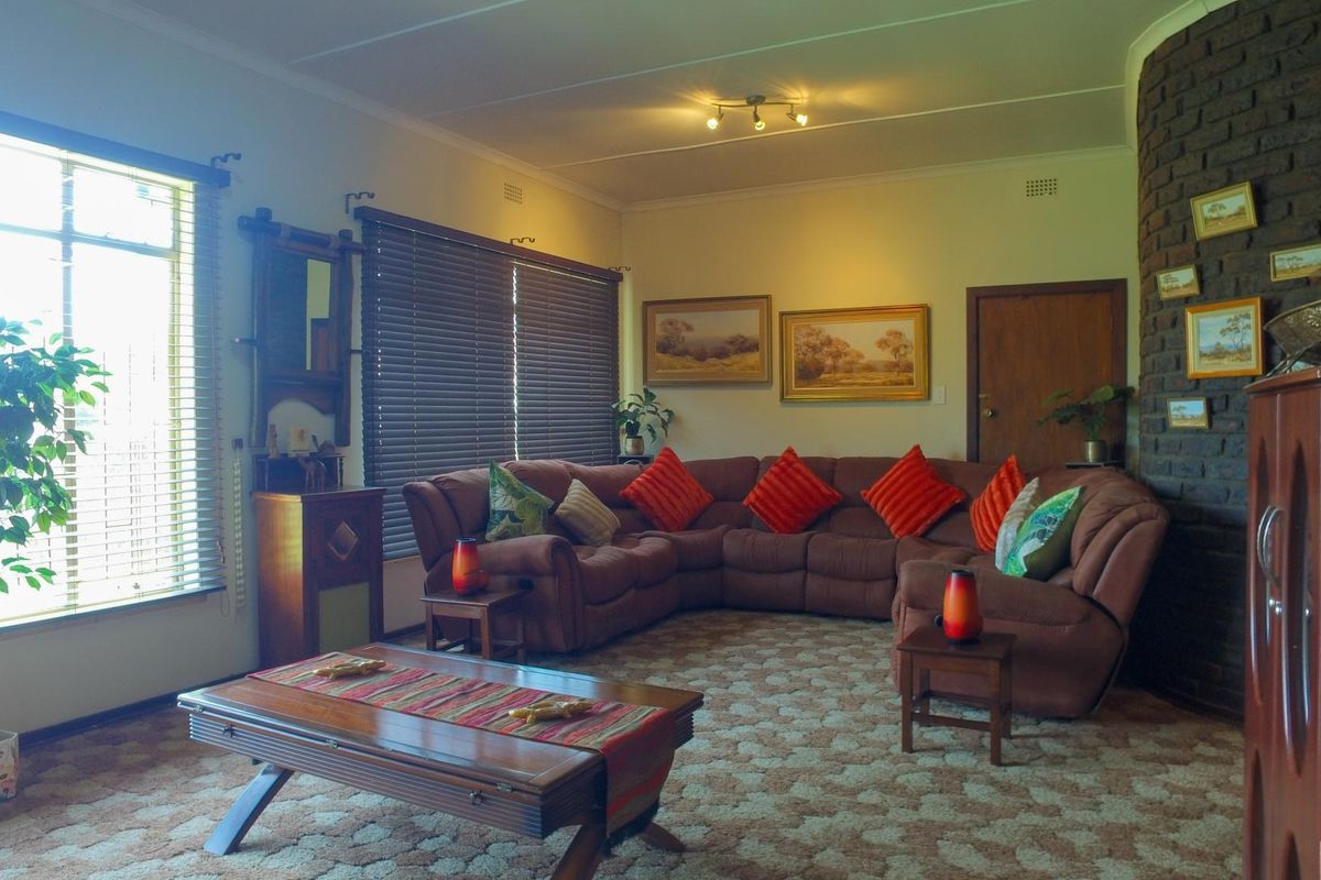 Spacious living room featuring a prominent brick fireplace, large windows with venetian blinds, and patterned carpet flooring.