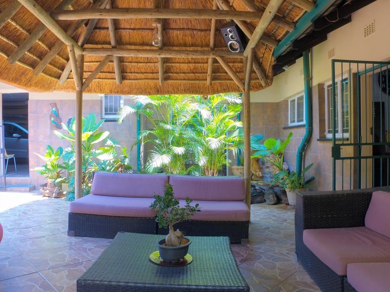 Covered outdoor patio area featuring a traditional thatched roof, tiled flooring, and decorative tiled wall accents, providing a comfortable space for relaxation.