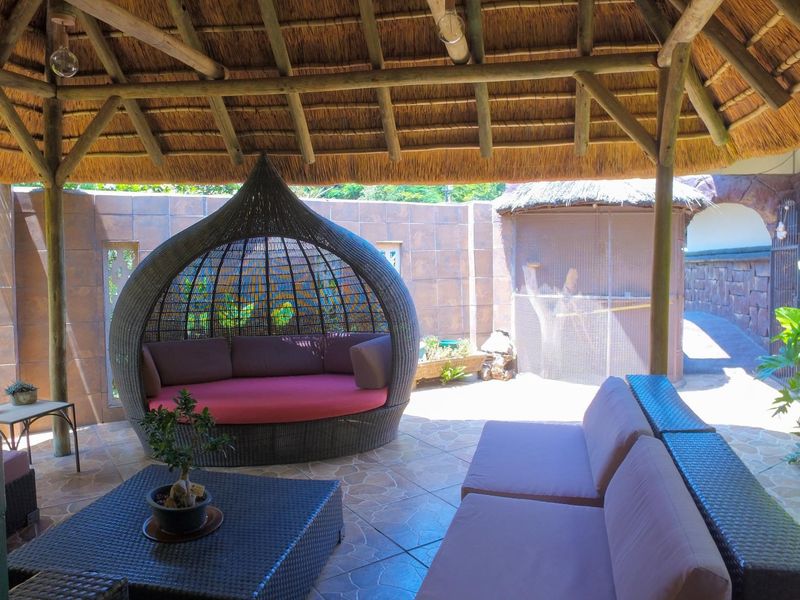 A covered outdoor patio area featuring a traditional thatched roof, timber support beams, and tiled flooring, providing a relaxed space for outdoor living.