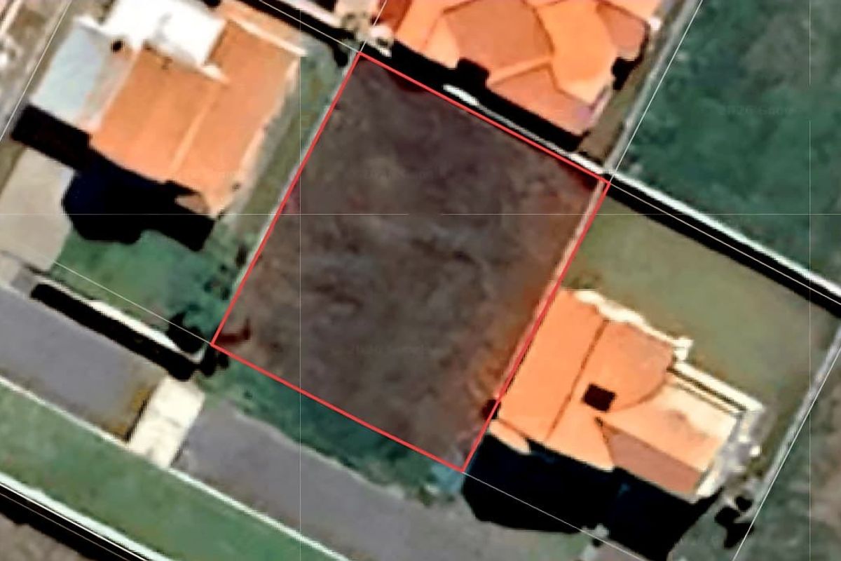 An aerial view of a vacant residential land plot situated between existing neighboring properties.