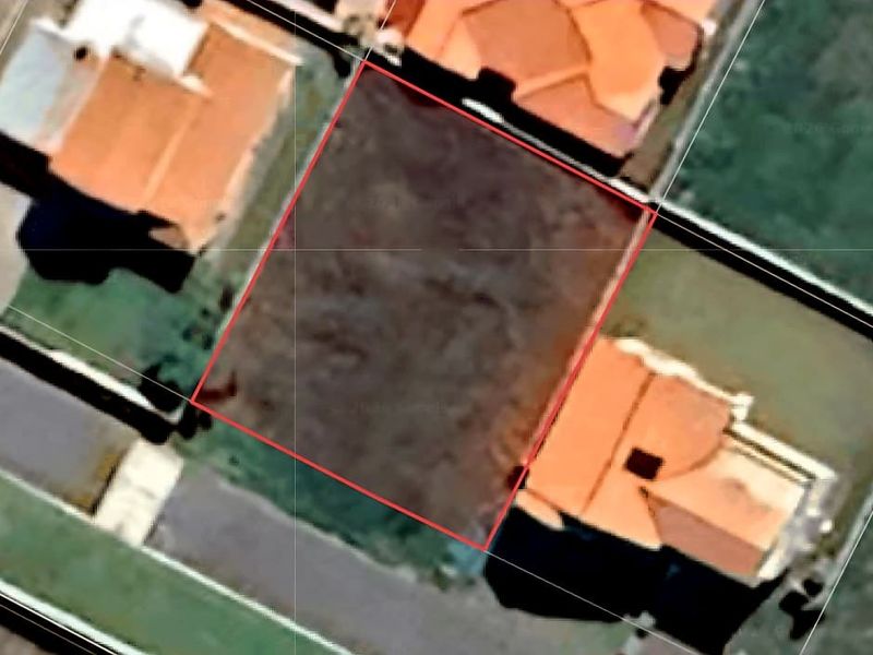 An aerial view of a vacant residential land plot situated between existing neighboring properties.