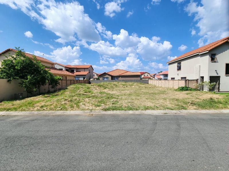 A vacant residential plot situated between existing homes, featuring a level grassed surface and established boundary walls in a suburban estate setting.
