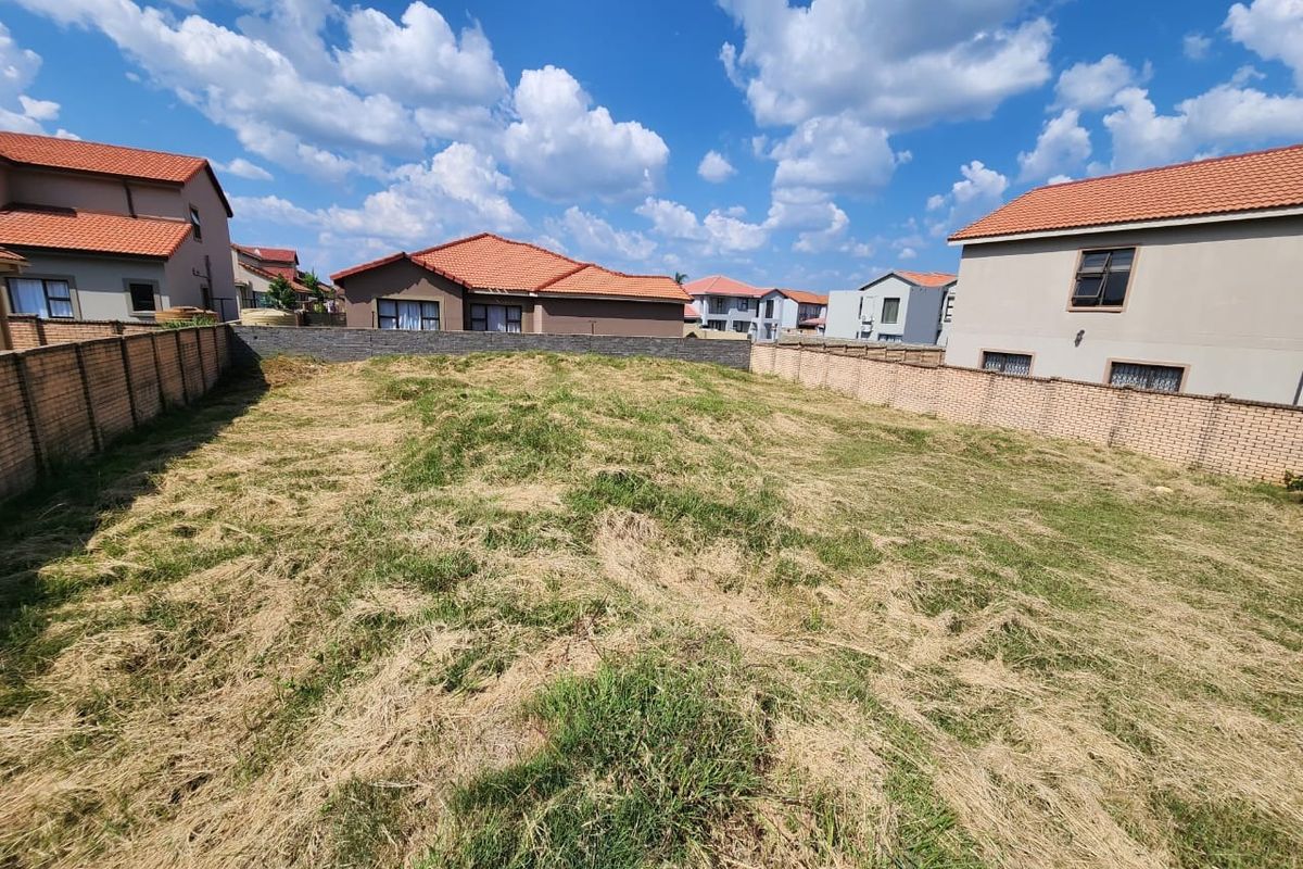 A vacant residential plot of land enclosed by brick boundary walls, situated within a developed suburban estate.