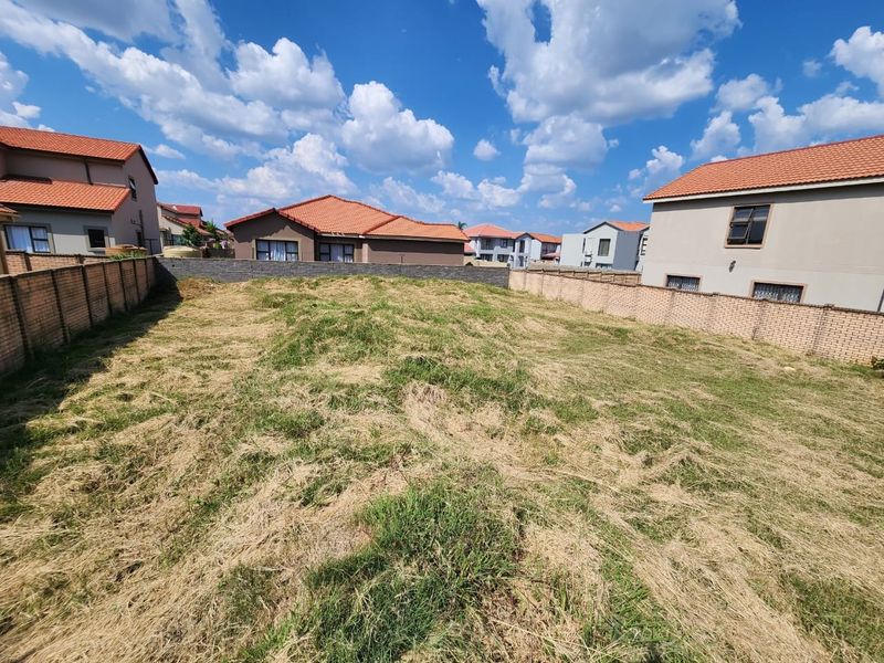 A vacant residential plot of land enclosed by brick boundary walls, situated within a developed suburban estate.