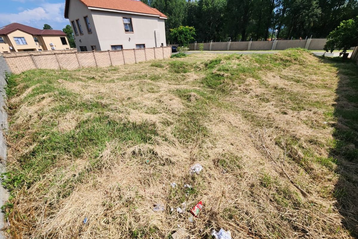 A vacant residential plot featuring perimeter brick walling and boundary fencing, currently covered in dry, overgrown grass.