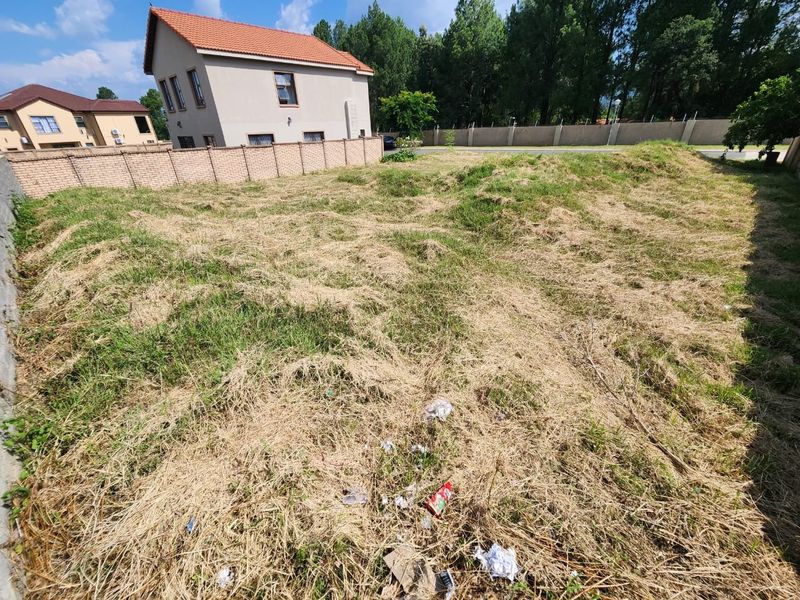 A vacant residential plot featuring perimeter brick walling and boundary fencing, currently covered in dry, overgrown grass.