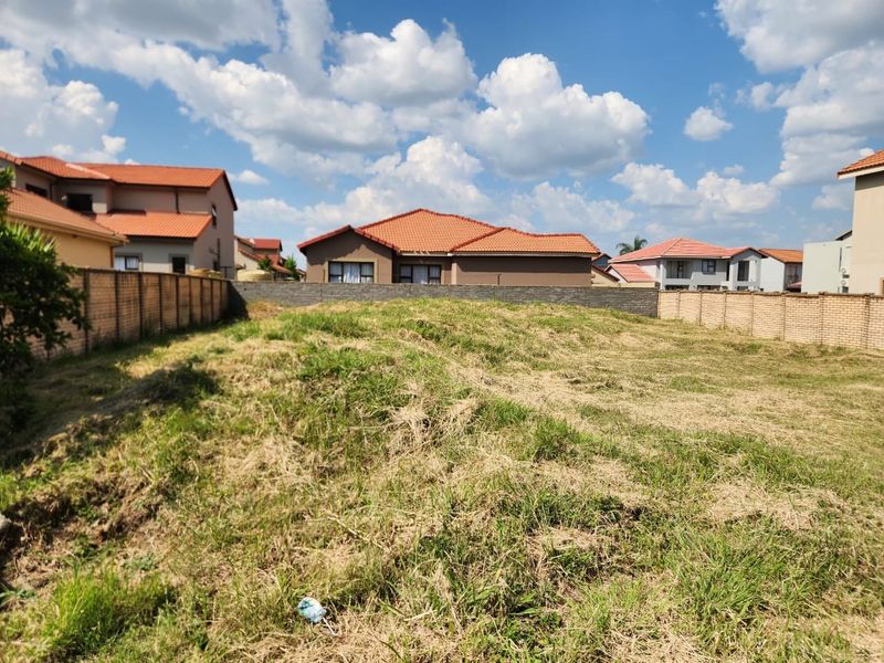 A vacant residential plot featuring a sloped grassy area enclosed by perimeter brick walls in a developed neighborhood.