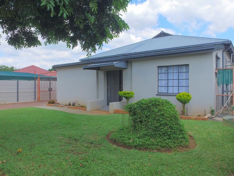 Front view of a single-story house featuring a metal roof, security-enhanced entrance, and a well-maintained lawn with perimeter walling.