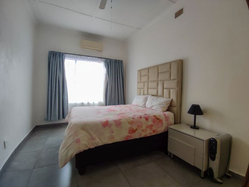 A functional bedroom featuring tiled flooring, a ceiling fan, and a wall-mounted air conditioning unit.