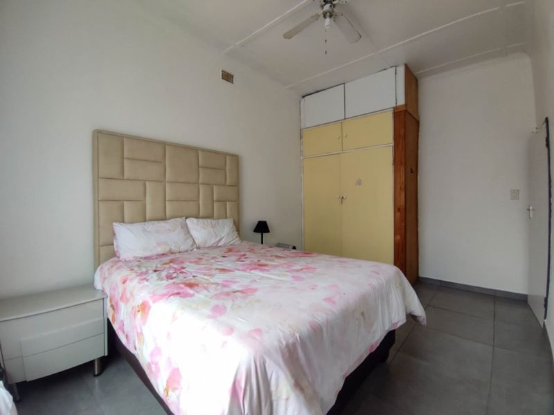 A bedroom featuring tiled flooring, a ceiling fan, and built-in cupboards with overhead storage compartments.