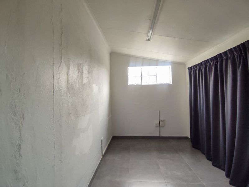 An empty bedroom featuring tiled flooring, a single window, and basic lighting, requiring cosmetic updates to the wall finishes.