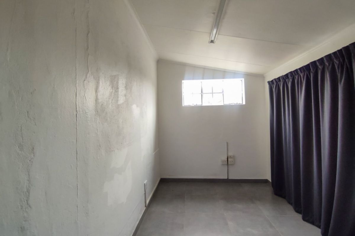 An empty bedroom featuring tiled flooring, a single window, and basic lighting, requiring cosmetic updates to the wall finishes.