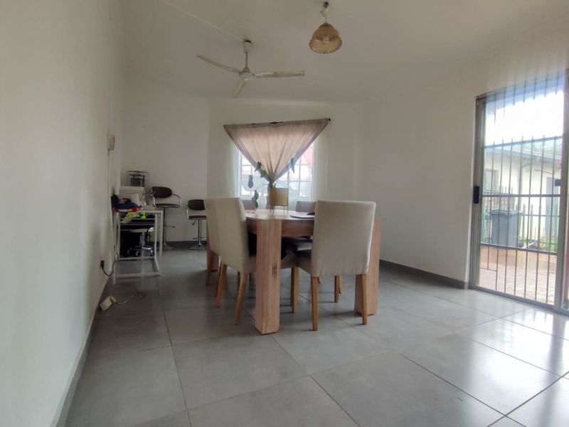 A bright dining area featuring large format floor tiles, a ceiling fan, and a sliding glass door with security gate leading to the exterior.