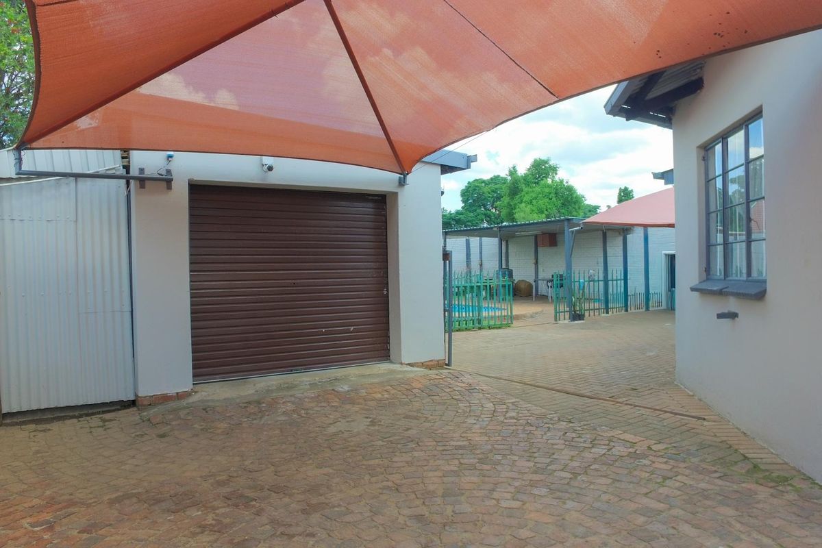 Rear exterior area featuring a paved driveway, roll-up garage door, and a shade sail covering the parking space.