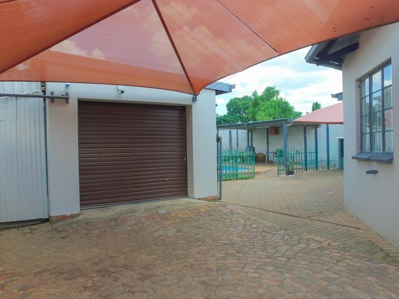 Rear exterior area featuring a paved driveway, roll-up garage door, and a shade sail covering the parking space.