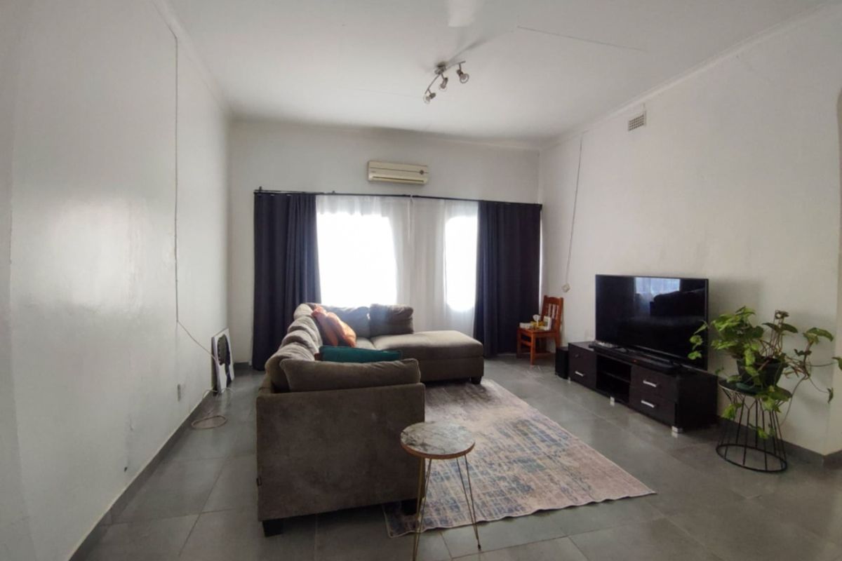 A spacious living room featuring neutral tiled flooring, a wall-mounted air conditioning unit, and ample natural light through the window.