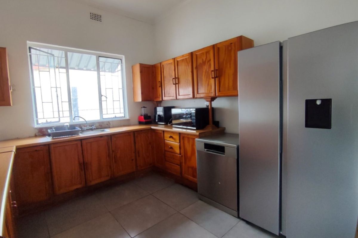 A functional kitchen featuring wooden cabinetry, laminate countertops, tiled flooring, and a stainless steel sink, offering a practical layout with ample storage space.