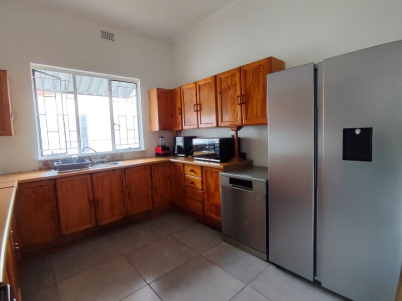 A functional kitchen featuring wooden cabinetry, laminate countertops, tiled flooring, and a stainless steel sink, offering a practical layout with ample storage space.
