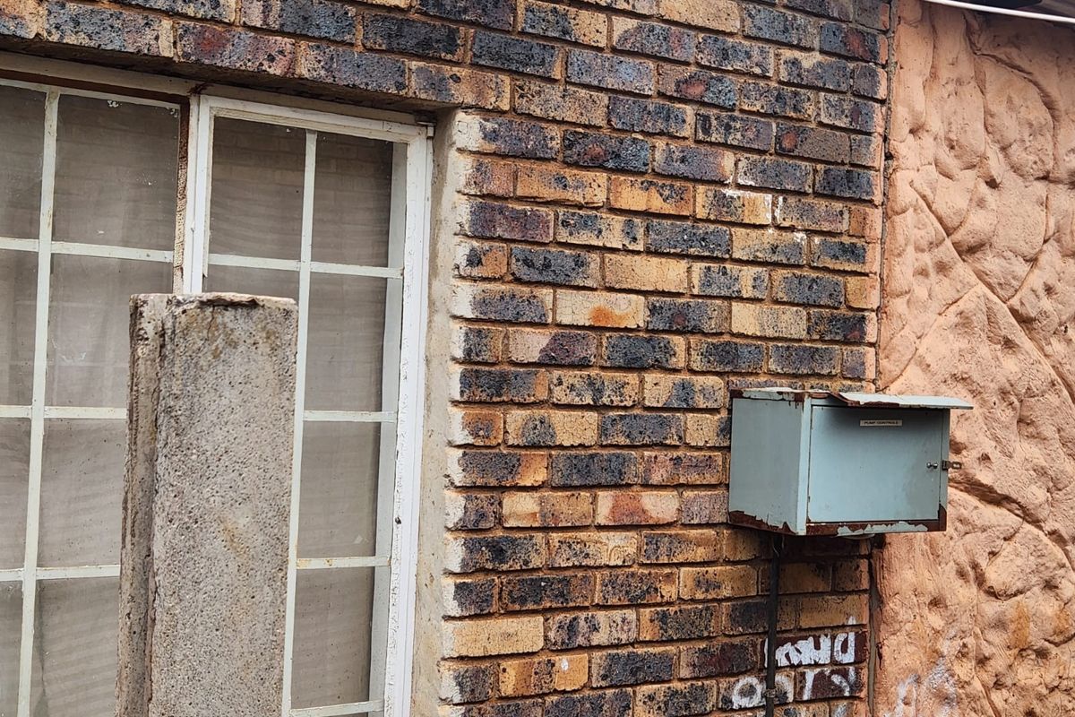 Exterior view of a brick and textured plaster wall featuring a steel window frame and a weathered metal utility box.