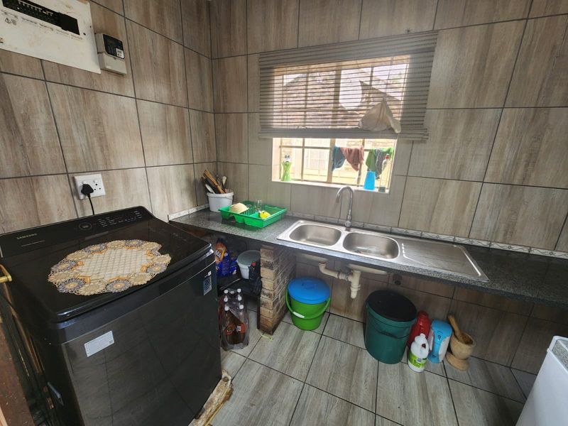 A functional laundry area featuring tiled walls and flooring, a double bowl stainless steel sink, and an integrated electrical distribution board.