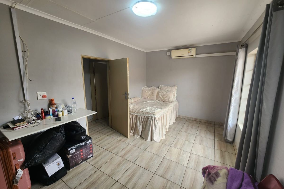A functional bedroom featuring tiled flooring, a wall-mounted air conditioning unit, and a standard doorway entrance.