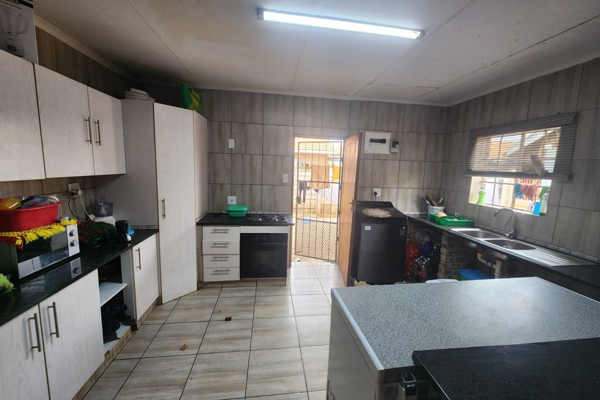 Functional kitchen featuring built-in cabinetry, granite countertops, integrated oven and hob, and tiled finishes throughout with direct access to the rear exterior.