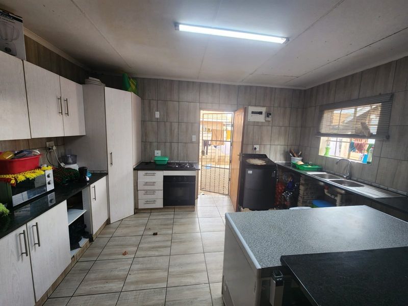 Functional kitchen featuring built-in cabinetry, granite countertops, integrated oven and hob, and tiled finishes throughout with direct access to the rear exterior.