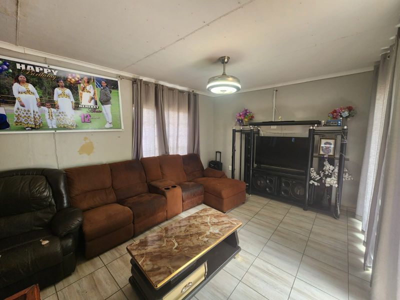 A living room featuring tiled flooring and a ceiling fan, currently showing signs of wear including wall surface damage.