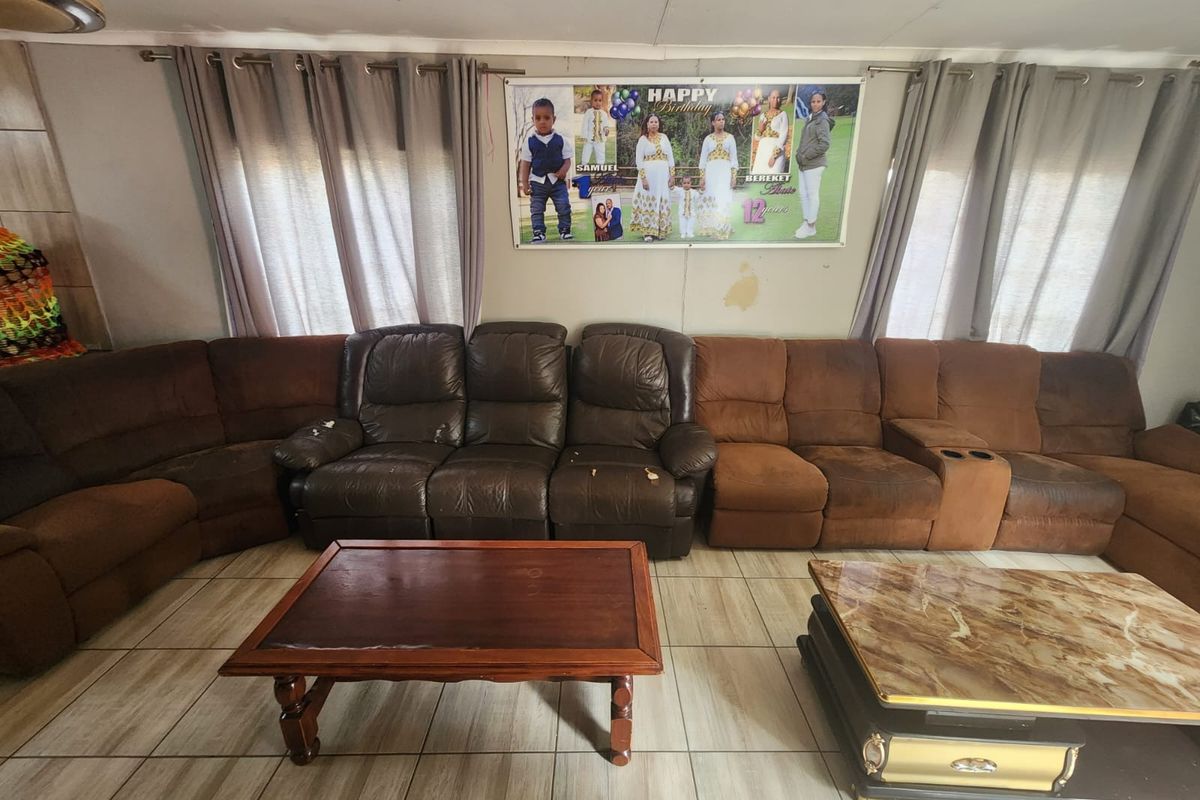 A living room featuring tiled flooring and curtain rods, showing signs of wear on the walls requiring maintenance.
