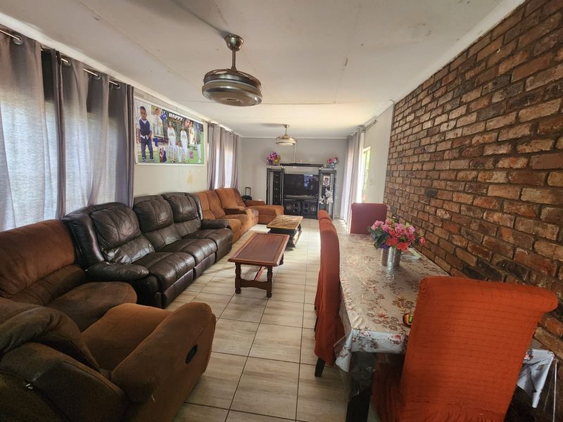 Spacious open-plan living and dining area featuring an exposed brick feature wall, tiled flooring, and dual ceiling fans.