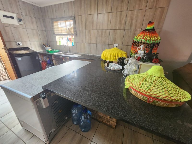 A functional kitchen featuring granite countertops, a double sink, and tiled wall finishes with neutral floor tiles.